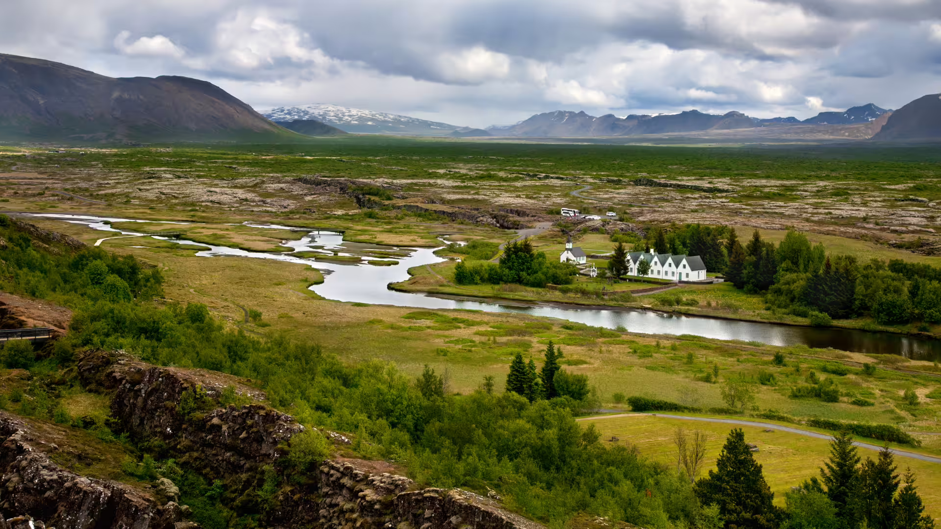 Aerial view of Þingvellir National Park, Iceland, with winding river, white church, green plains and snow-capped mountains