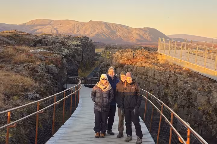 Four tourists posing on a wooden bridge at Þingvellir rift valley, Iceland, with snow-capped mountains at sunset