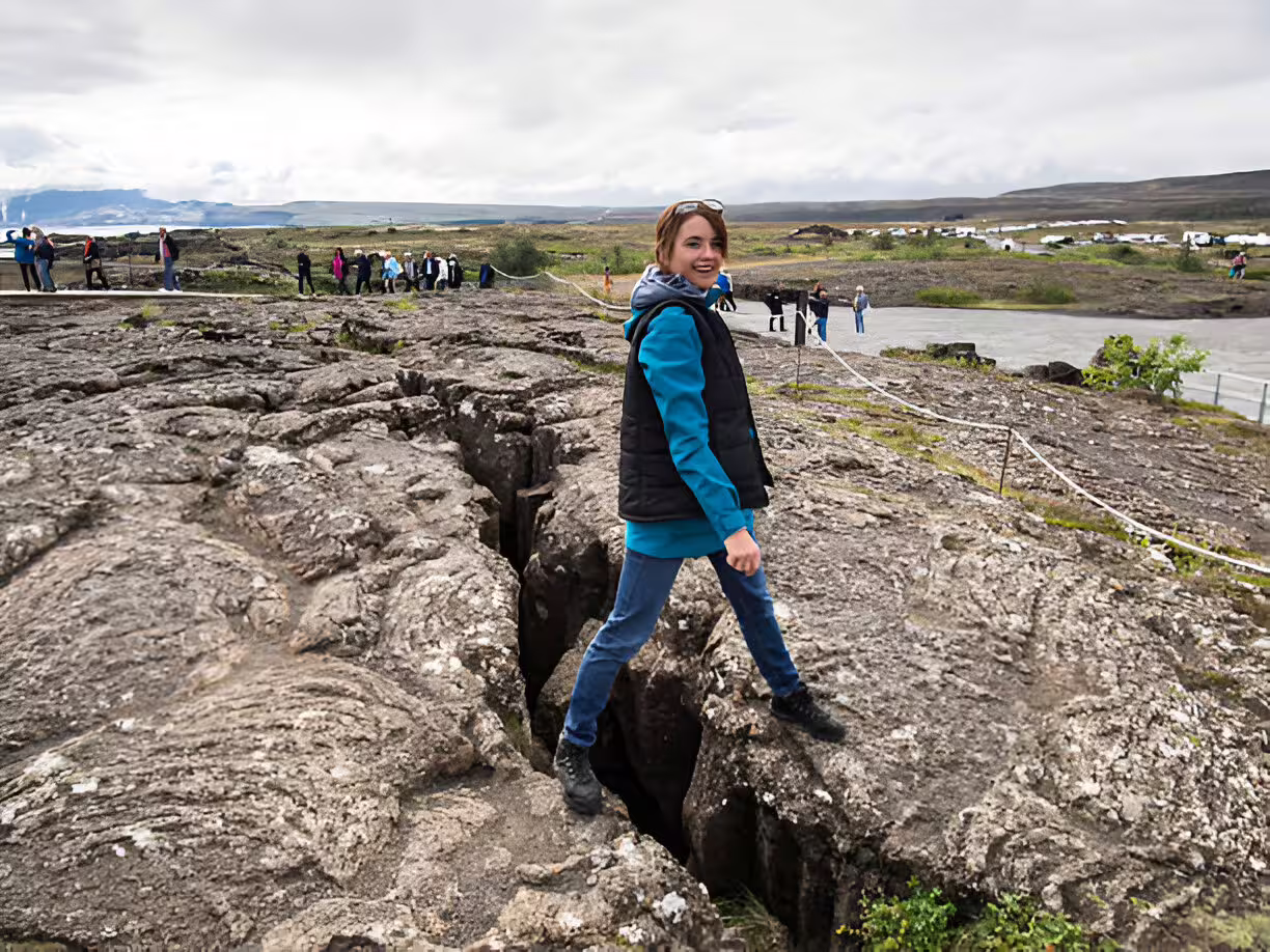 Tourist straddling tectonic plate fissure at Thingvellir National Park on Golden Circle tour Iceland