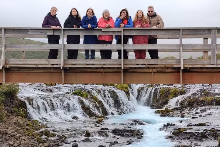 Group of seven tourists posing on wooden bridge over Bruarfoss waterfall on Golden Circle tour