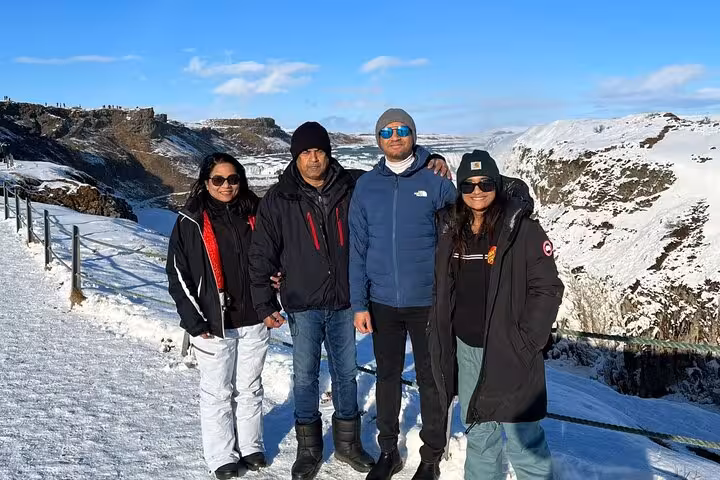 Four tourists posing at snowy Gullfoss waterfall canyon viewpoint on Iceland's Golden Circle tour