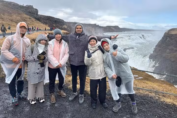 Group of tourists in rain ponchos posing at Gullfoss waterfall on Iceland's Golden Circle tour
