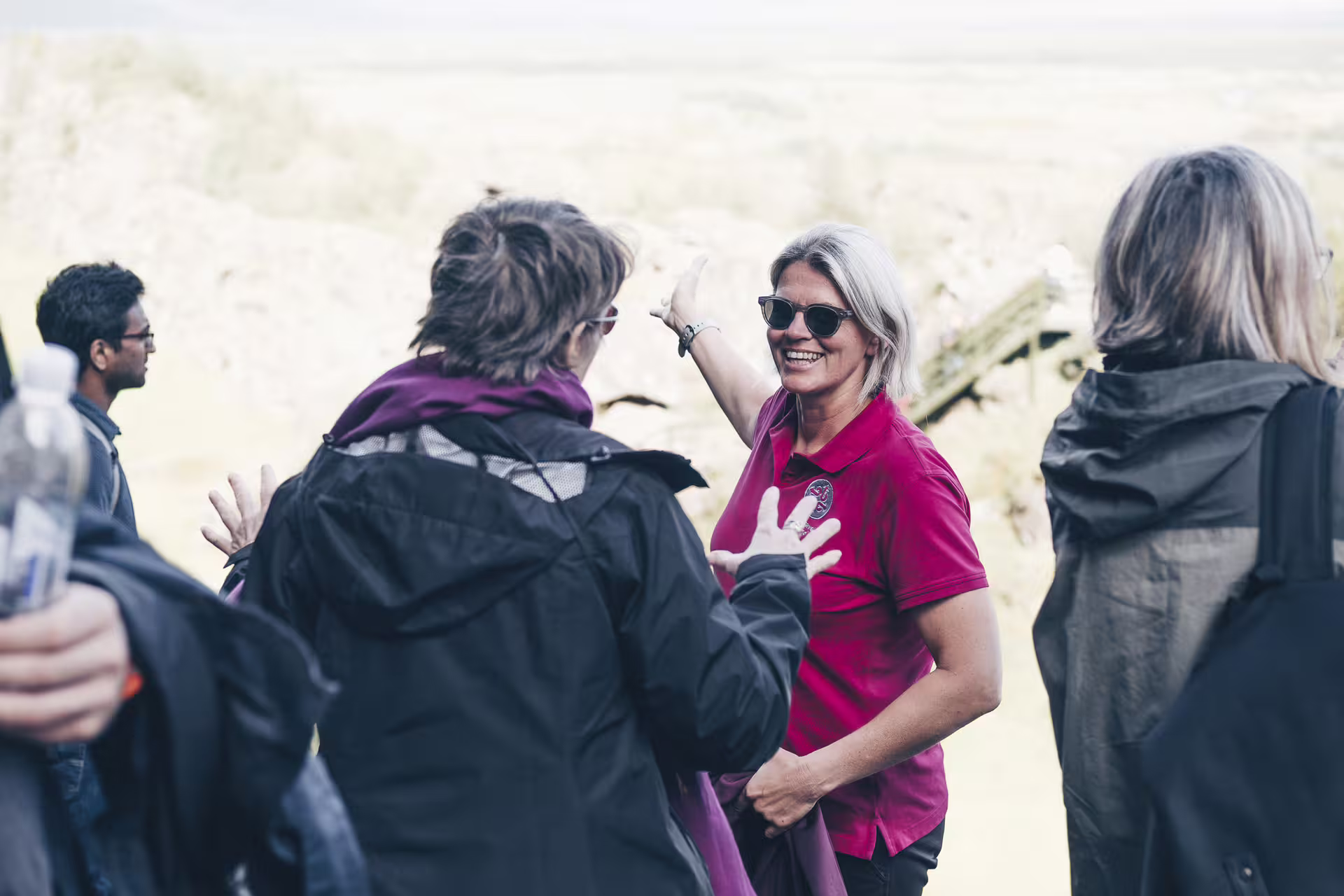 Tour guide in red polo shirt smiling and gesturing to group outdoors on Golden Circle Iceland tour