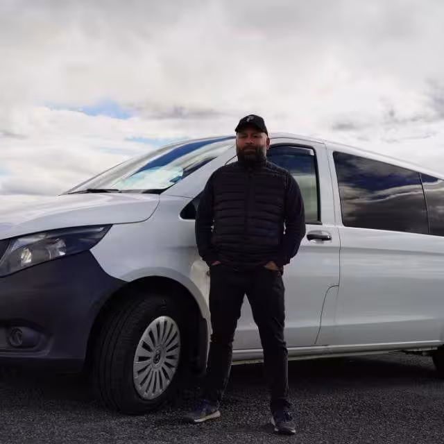 Tour guide standing beside a silver Mercedes van under cloudy Icelandic skies