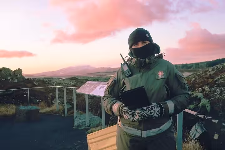 Tour guide in winter gear holding tablet at scenic Iceland viewpoint during pink sunset