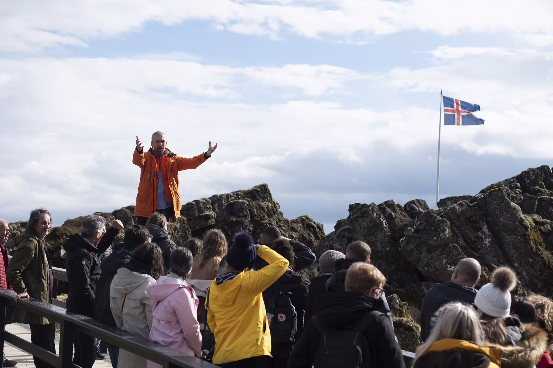 Tour guide in orange jacket addresses crowd at Þingvellir with Icelandic flag, Golden Circle Iceland