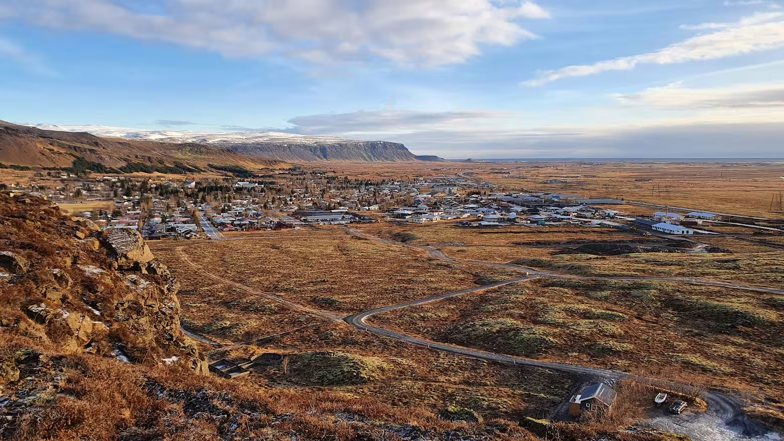 Aerial view of small Icelandic town on Golden Circle route with volcanic landscape and snow-capped cliffs
