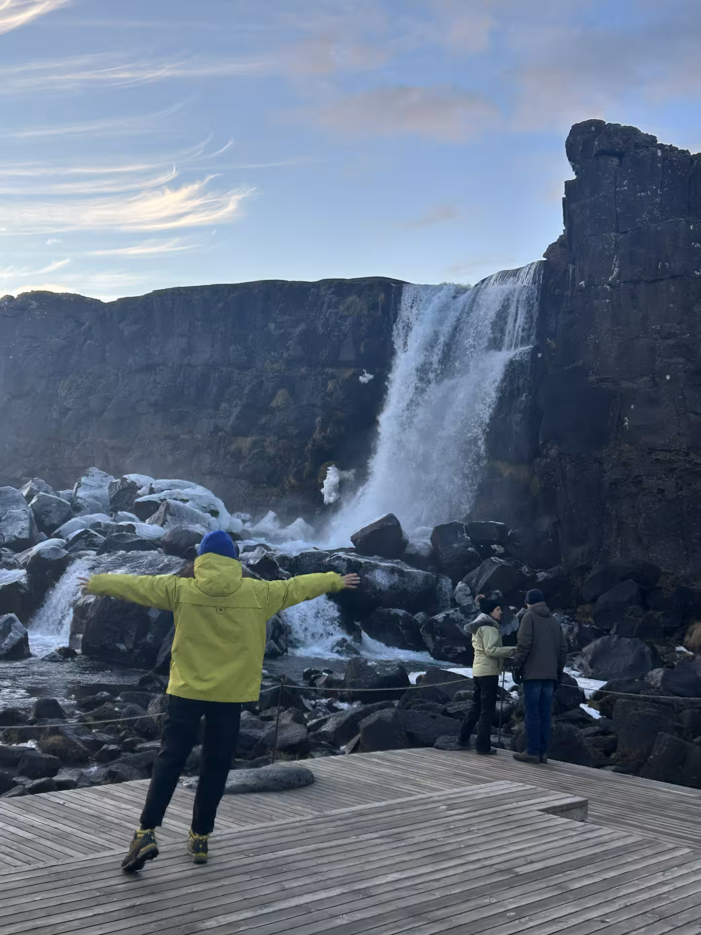 Tourist in yellow jacket with arms outstretched at Öxará waterfall on Iceland Golden Circle tour