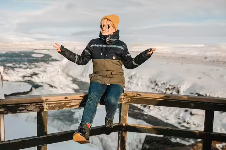 Traveler sitting on viewpoint railing overlooking snowy Golden Circle landscape in Iceland