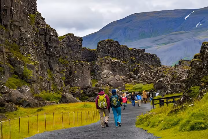 Tourists walking a paved path through dramatic lava rock formations on Iceland's Golden Circle route
