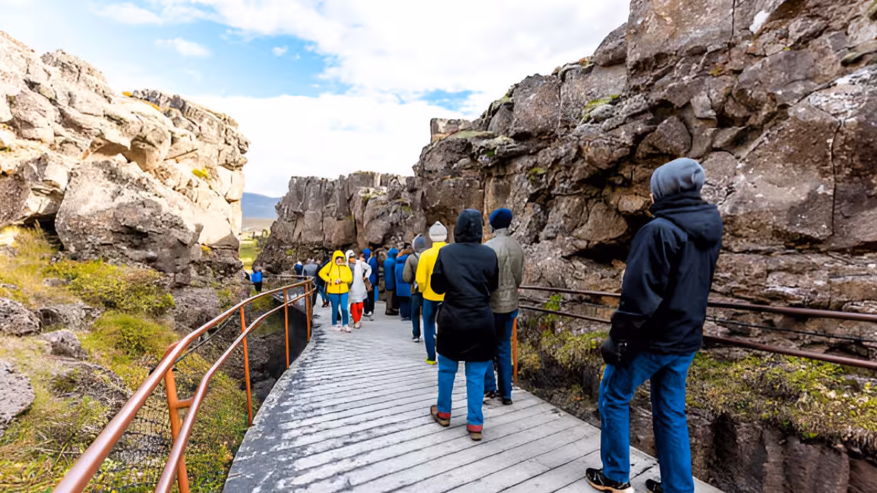 Tourists walking wooden boardwalk through Þingvellir tectonic rift canyon on Golden Circle tour Iceland