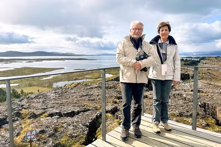 Couple standing on wooden viewpoint overlooking Þingvellir lake and lava fields on Iceland Golden Circle tour