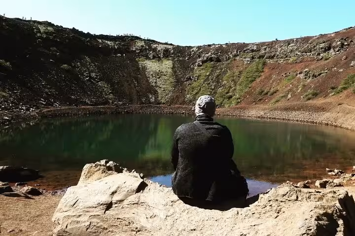 Person sitting on rock overlooking green volcanic crater lake on Iceland's Golden Circle tour