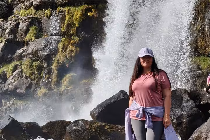 Woman in pink shirt posing in front of a powerful waterfall on Iceland's Golden Circle tour