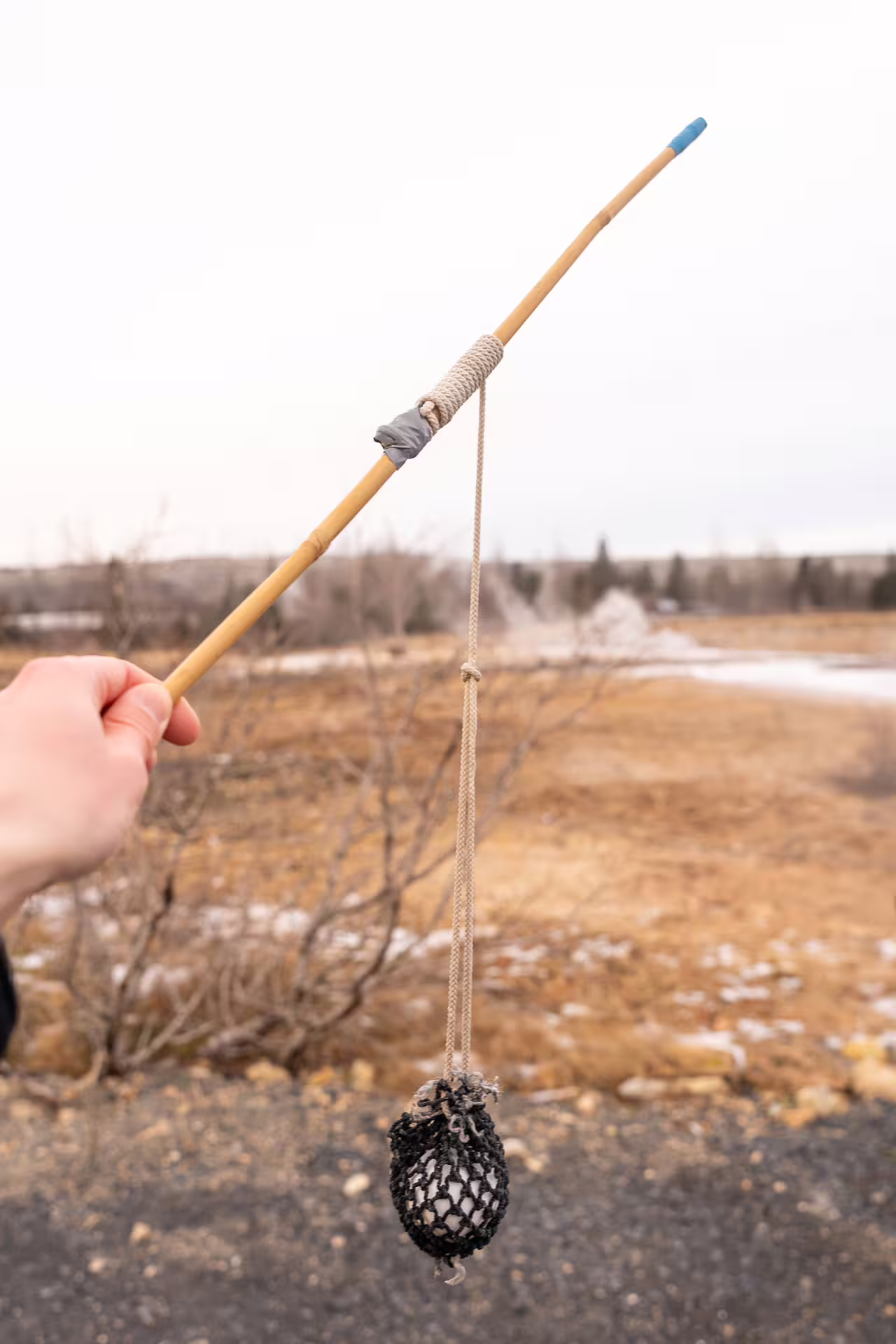 Hand holding a bamboo stick with rope and netted weight used in Icelandic golden circle tour activity