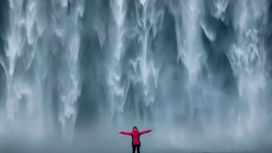 A person standing in front of a large waterfall with arms outstreched