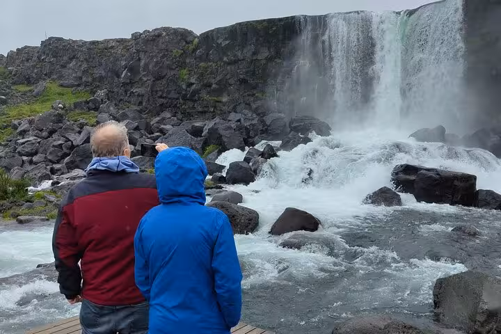 Two visitors in rain jackets viewing a powerful waterfall on Iceland's Golden Circle tour