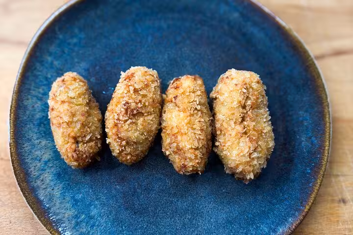 Four golden croquettes on a blue plate, highlighting hands-on tapas making in an authentic Barcelona cooking class.