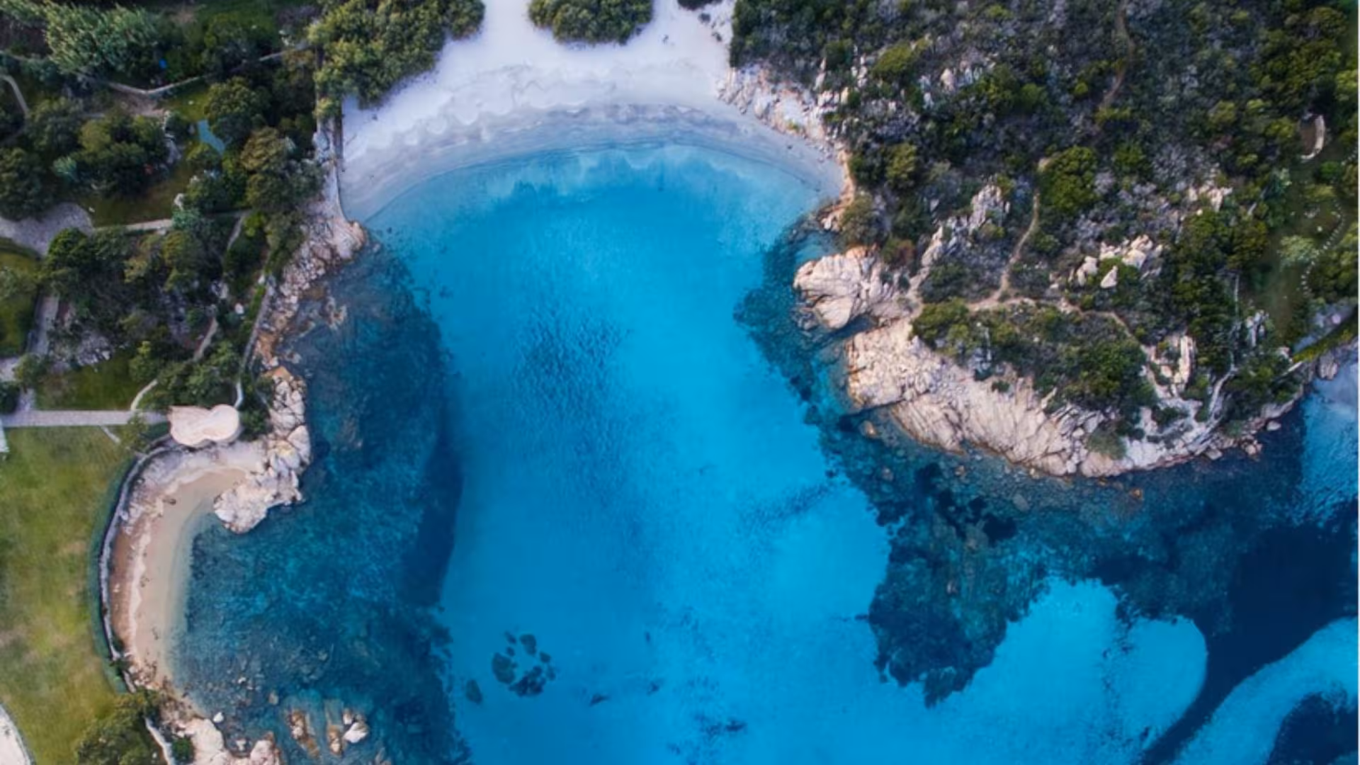 Stunning aerial shot of a secluded cove in Golfo Aranci with clear blue waters surrounded by rocky cliffs and greenery.