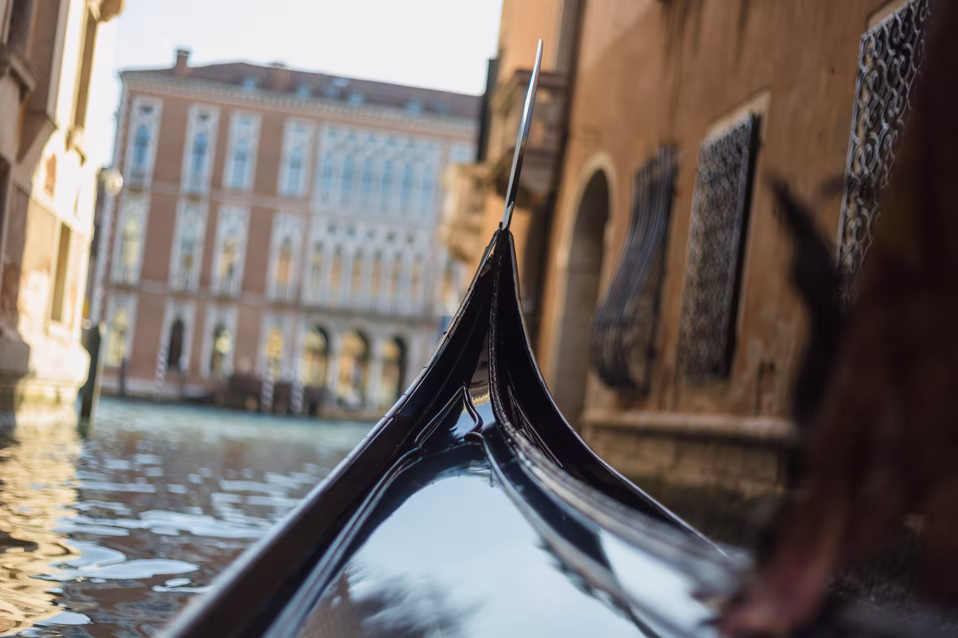 Close-up of a gondola prow gliding along Venice's Grand Canal, surrounded by historic architecture.