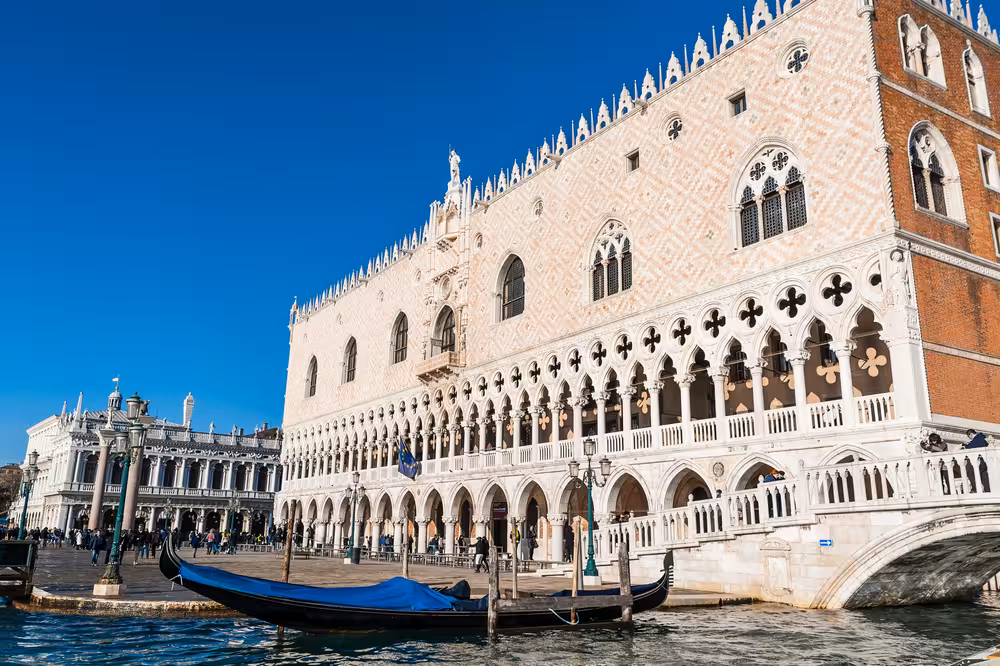Experience a gondola ride alongside the historic Doge's Palace on a sunny day in Venice.