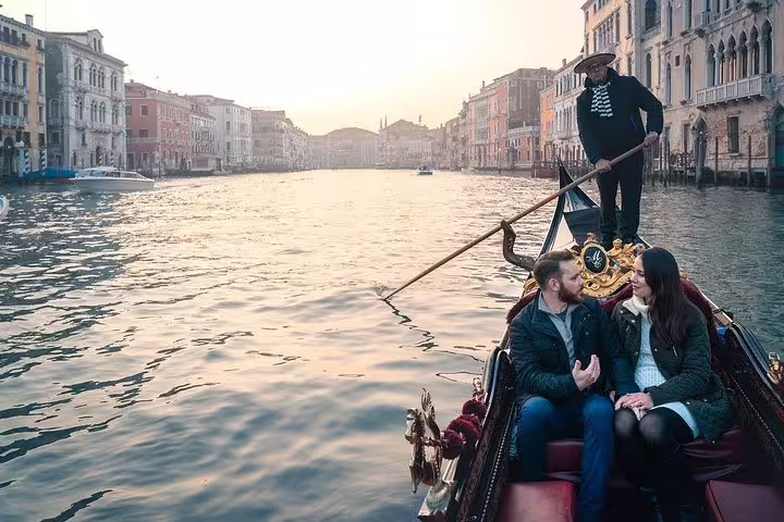 Couple enjoying a gondola ride at sunset on the Grand Canal with picturesque Venetian architecture.