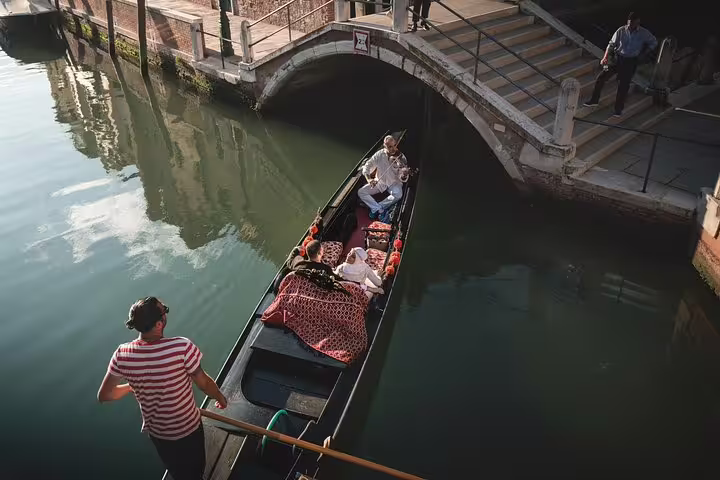 Gondola glides under a bridge with a couple enjoying a violin serenade and champagne in Venice.