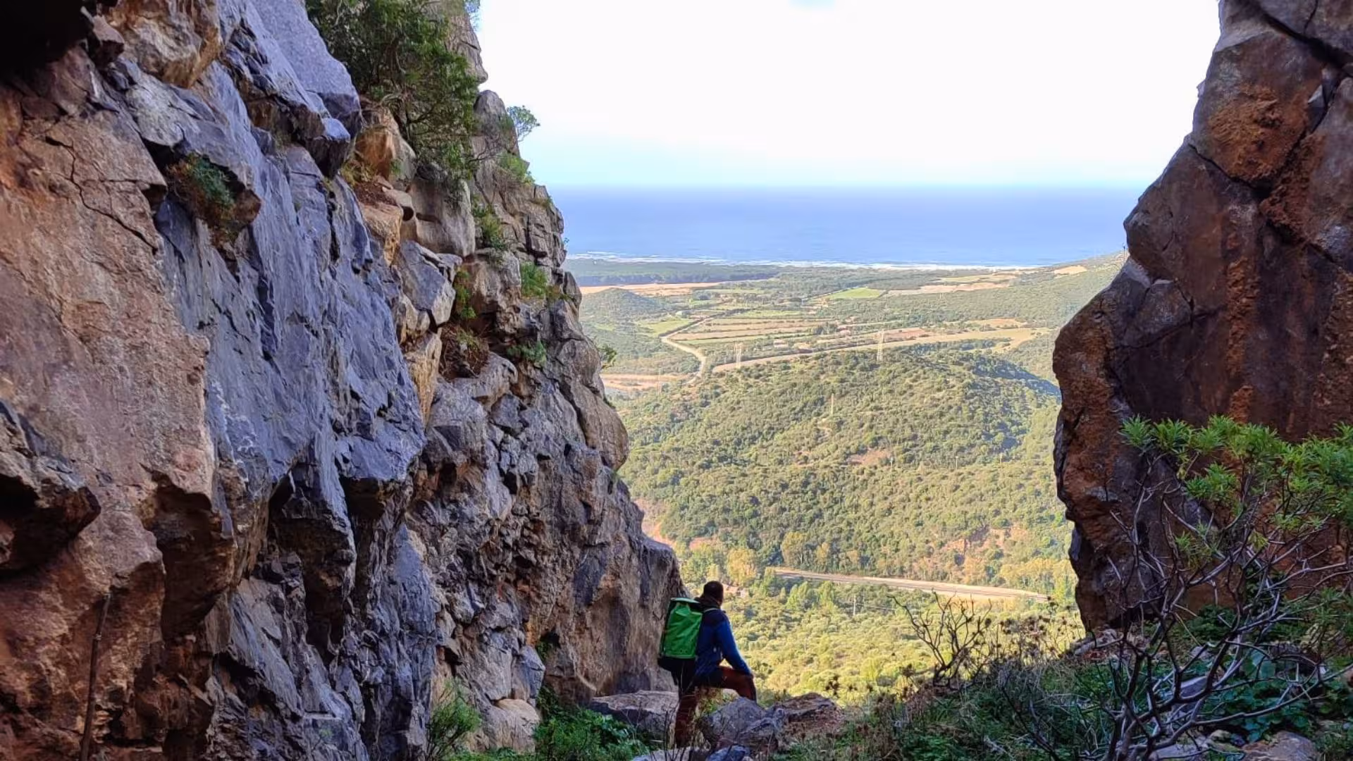 Adventurer explores rugged Monte San Giovanni canyon with panoramic views of Sardinia's lush landscape and coastline.