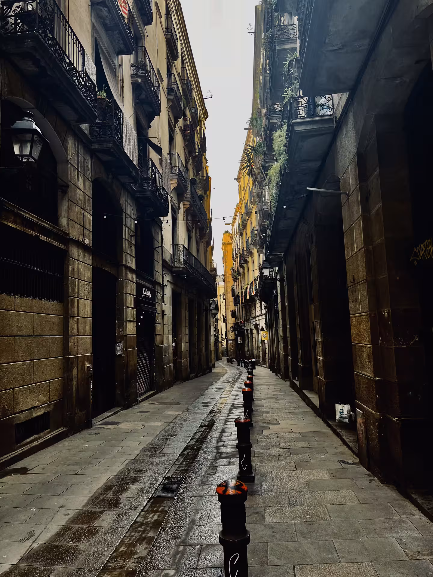 Narrow Gothic Quarter street near Barcelona Cathedral, wet cobblestones and balconies on Sucesos Locales walk