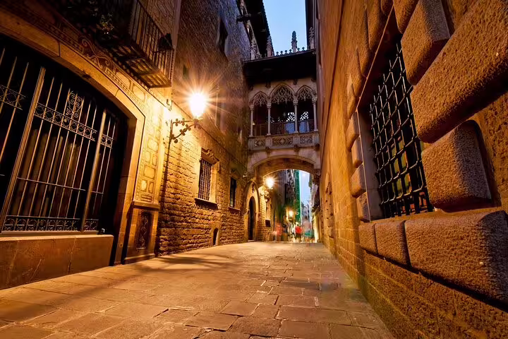 Narrow Gothic Quarter alley at night with glowing lanterns and medieval stone bridge arch in Barcelona