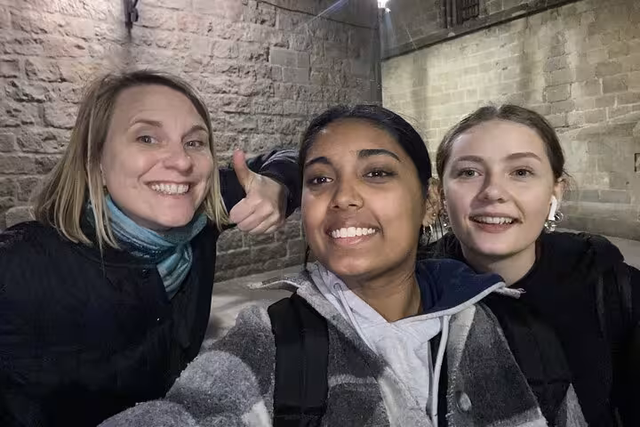 Three smiling women taking a selfie at night near ancient stone walls in Barcelona's Gothic Quarter