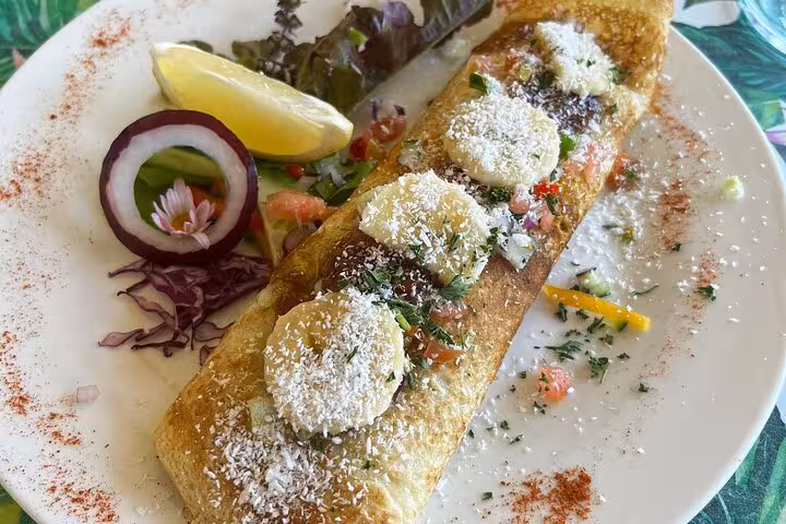 Delicious gourmet crepe with banana slices and coconut, served with fresh vegetables and a lemon wedge.
