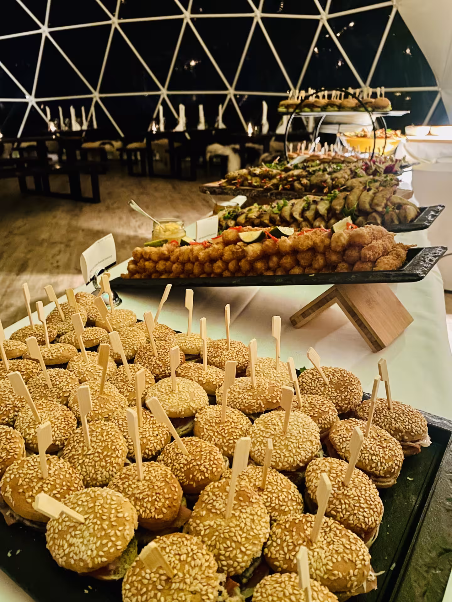 Elegant gourmet food pairing buffet with mini sliders and crispy bites served inside a lakeside dome venue