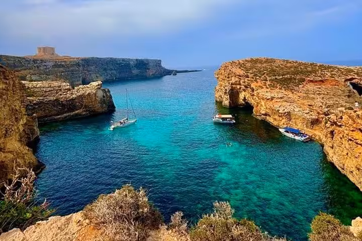 Gozo coastline lagoon with turquoise water and boats, stop on Half Day Malta tour to Comino Blue Lagoon caves
