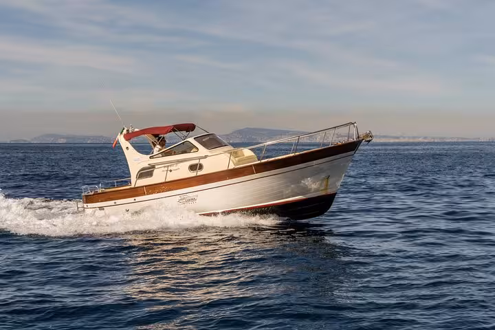 Elegant Gozzo 850 boat cruising the clear waters between Sorrento and Amalfi with a scenic coastline in the background.