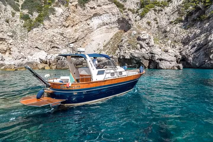 Gozzo Apreamare boat navigating crystal-clear waters near rocky cliffs on a Capri and Positano private tour.