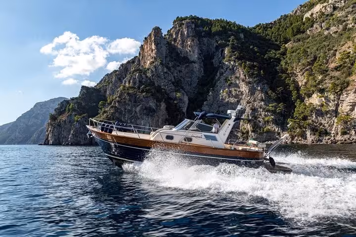 Gozzo Apreamare boat cruising past dramatic cliffs under a blue sky on the Capri and Positano private tour.