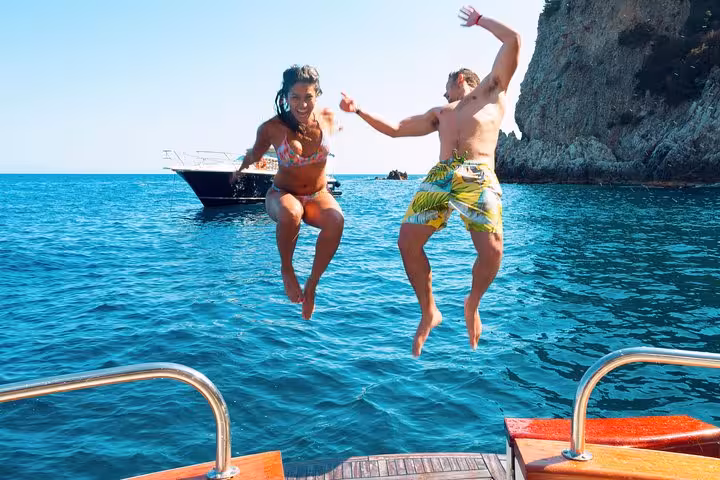 Two people joyfully jump into the crystal-clear waters from a Typical Gozzo boat on a Sorrento to Amalfi tour.