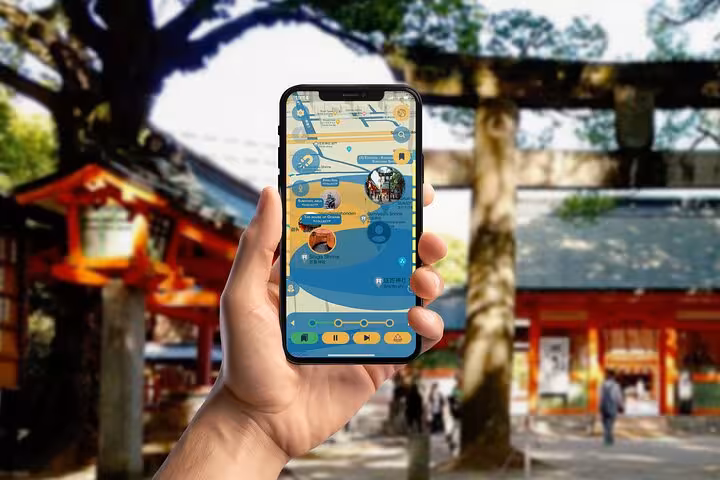 Hand holding smartphone with GPS walking tour app map near a traditional Fukuoka shrine torii gate