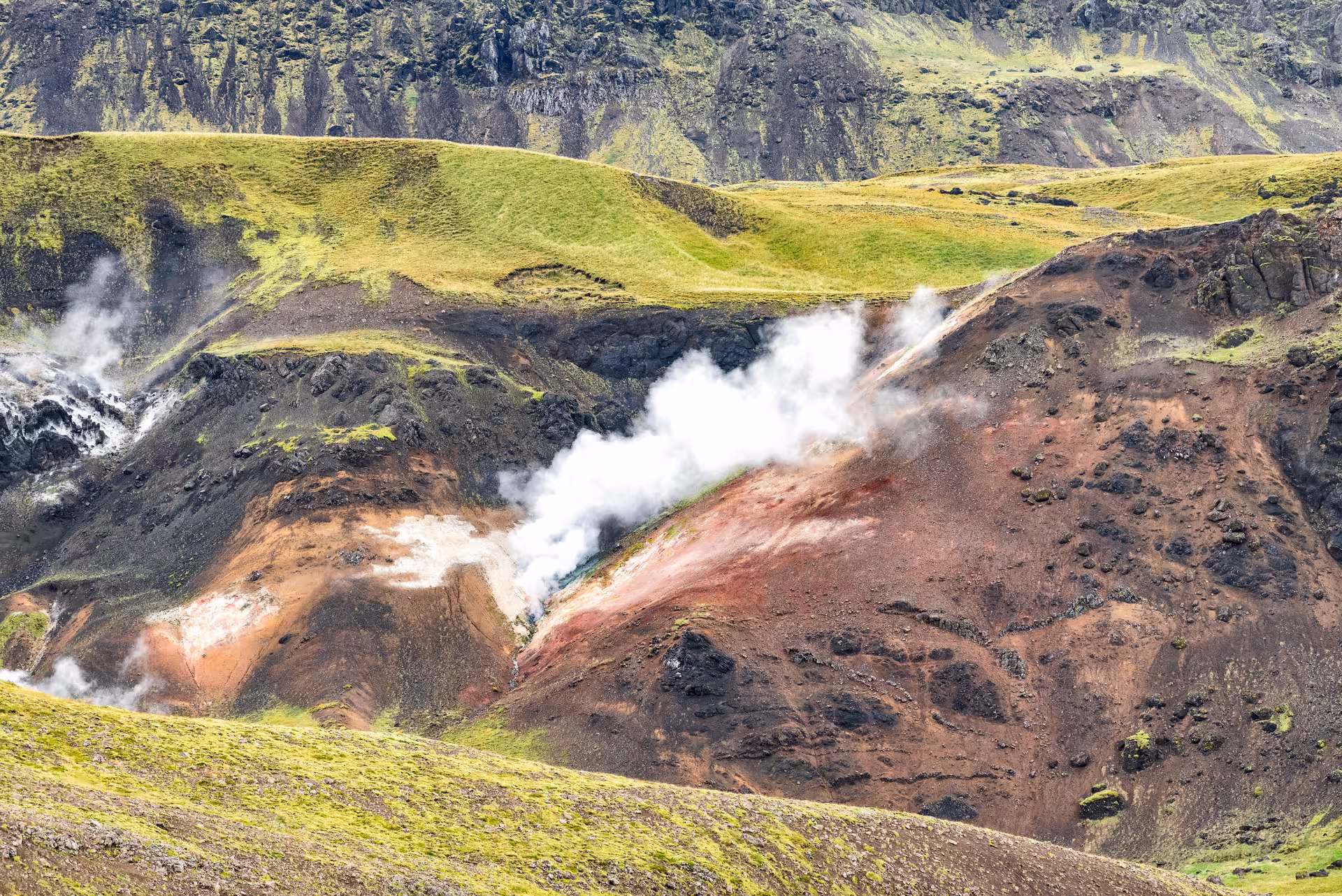 Close-up of Grændalur geothermal area with billowing steam over red volcanic slopes on private hike