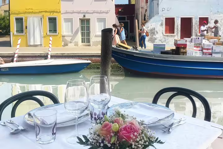 Outdoor lunch table by Burano canal on private Grand Canal boat tour to Murano and Burano, Venice