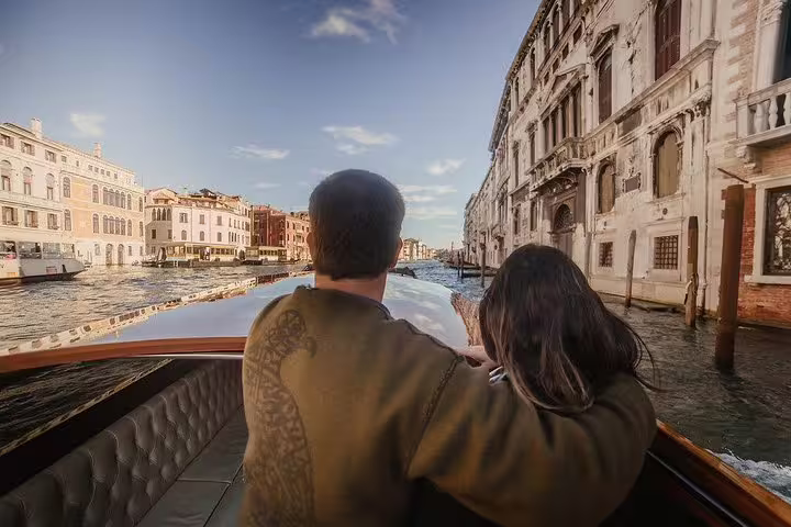 Couple enjoys a scenic Grand Canal view from a boat, highlighting Venice's stunning architecture on a shared tour.
