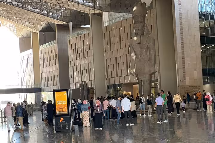 Visitors inside the Grand Egyptian Museum Cairo atrium beneath a towering statue on Hurghada to Cairo tour