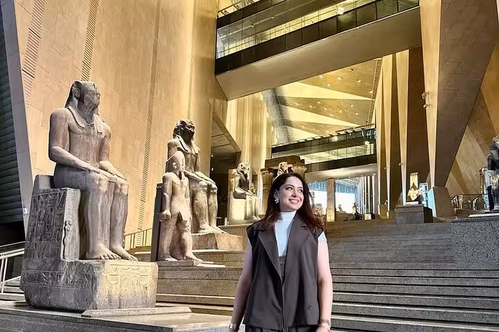 Traveler at Grand Egyptian Museum entrance hall beside colossal statues, before Giza Pyramids and Sphinx tour