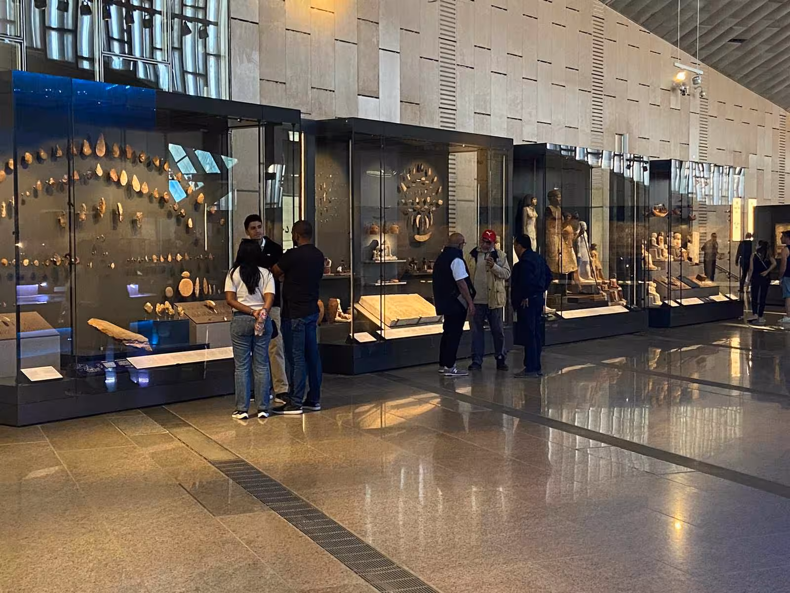 Grand Egyptian Museum gallery with ancient Egyptian artifacts and visitors, part of Giza Pyramids tour with lunch