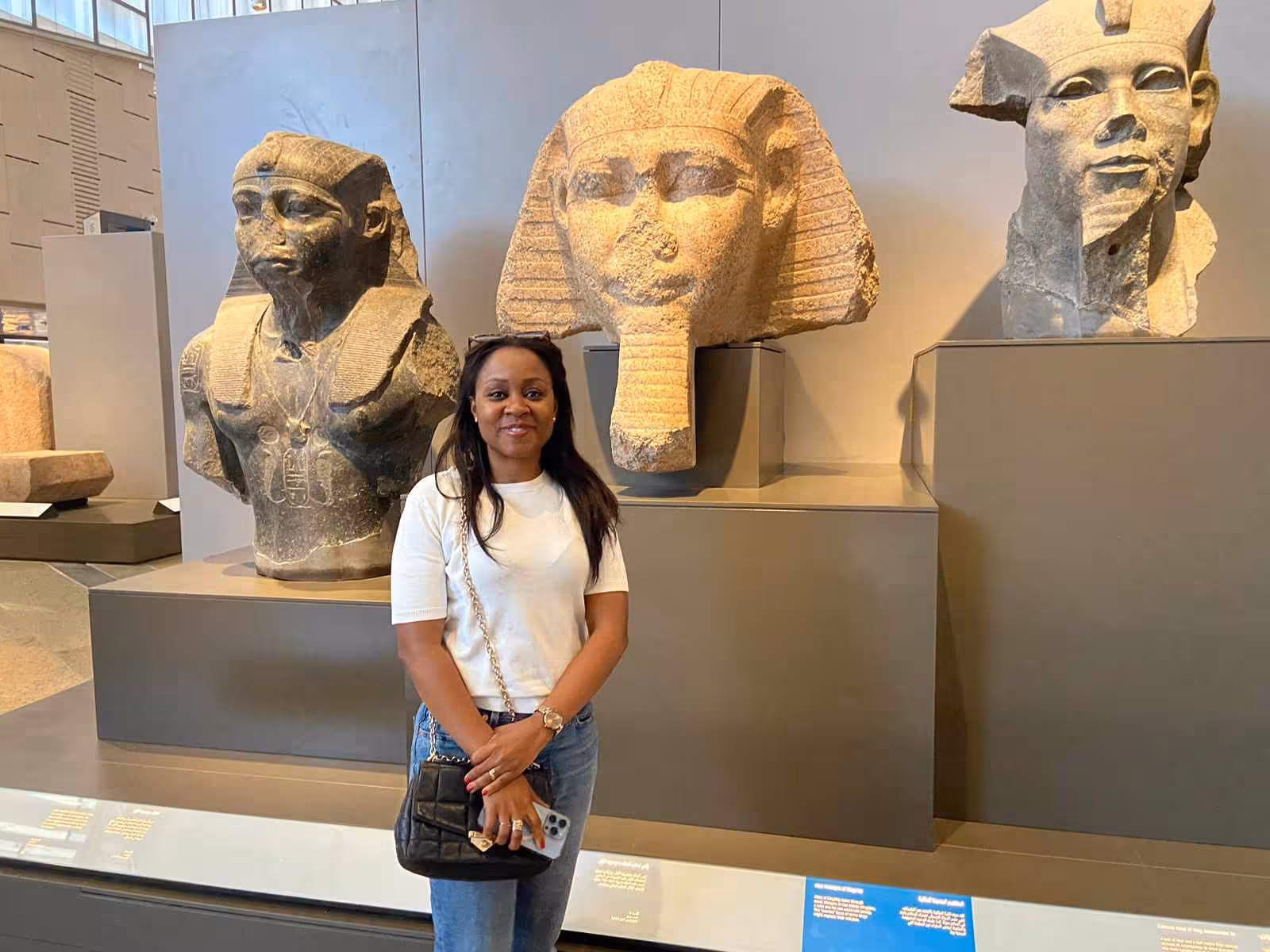 Visitor posing with colossal pharaoh statue heads inside Grand Egyptian Museum, Cairo guided tour highlight