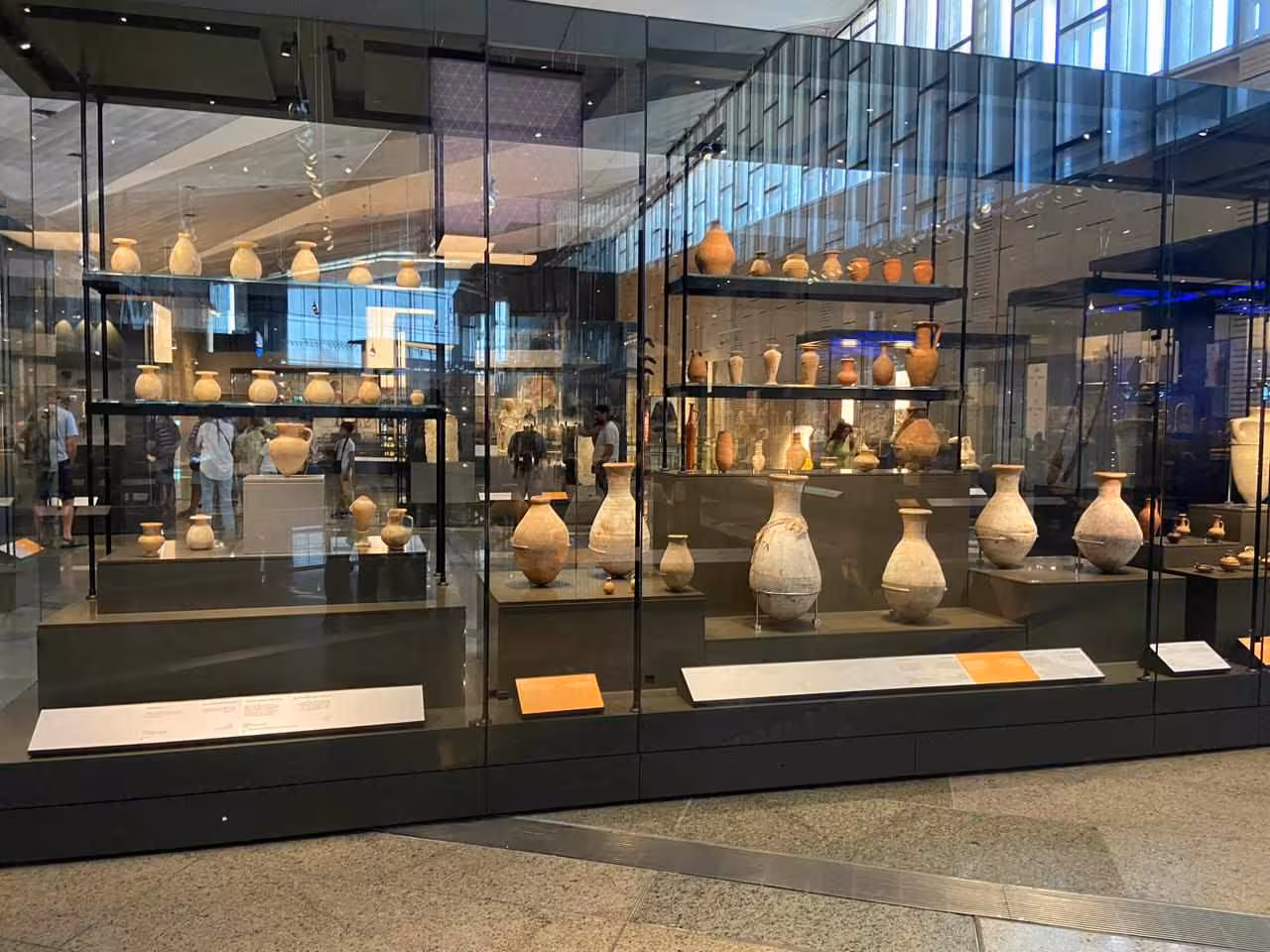 Grand Egyptian Museum pottery gallery in Cairo with ancient jars and vases displayed in modern glass cases