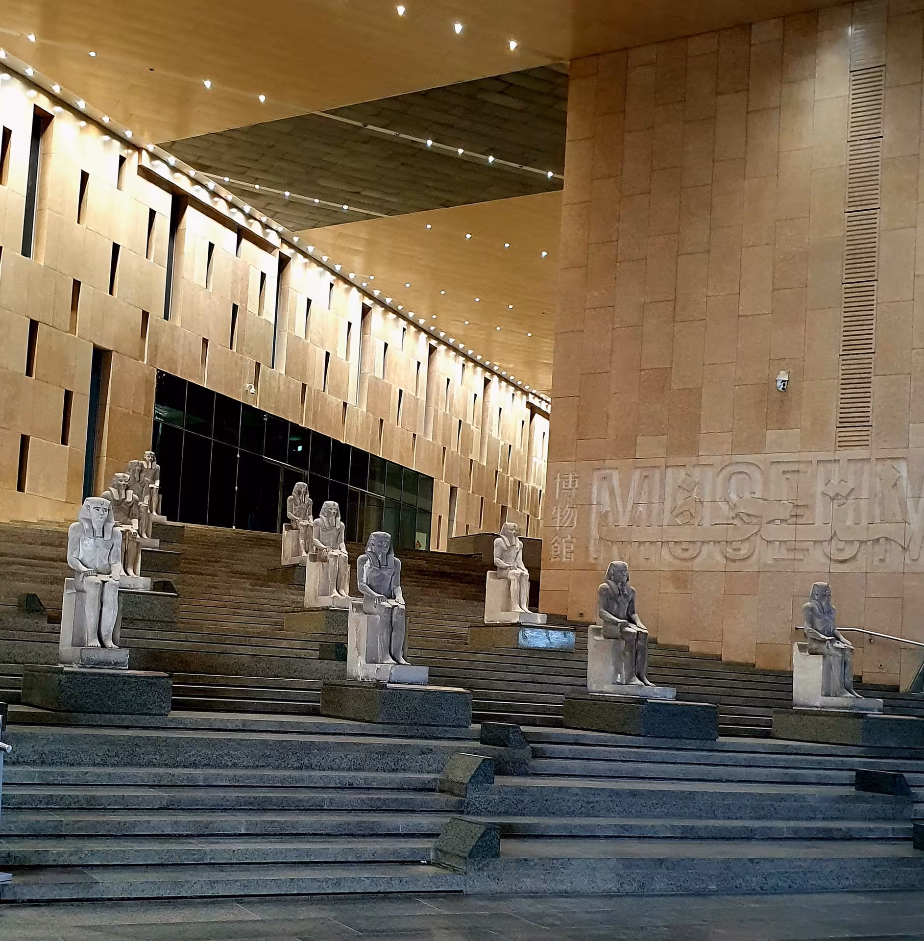 Ancient Egyptian statues lining grand staircase inside the Grand Egyptian Museum at night