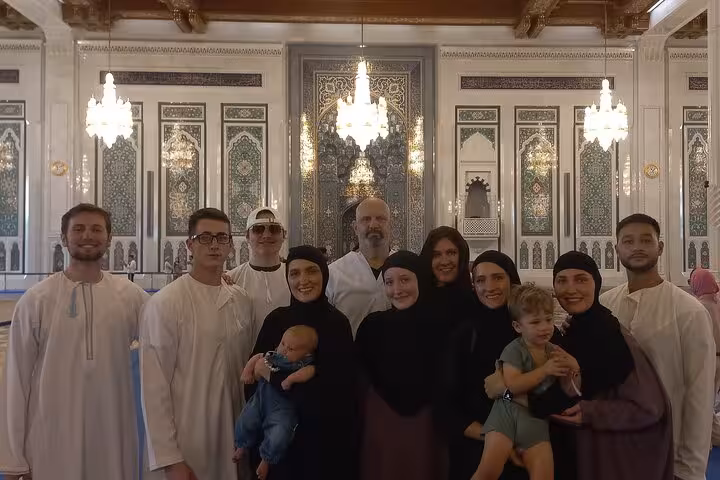 Tour group posing inside ornate Grand Mosque Muscat with intricate Islamic tilework and chandeliers