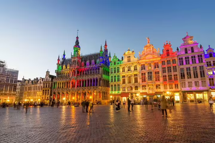 Grand Place Brussels illuminated with colorful lights at dusk with tourists exploring the cobblestone square